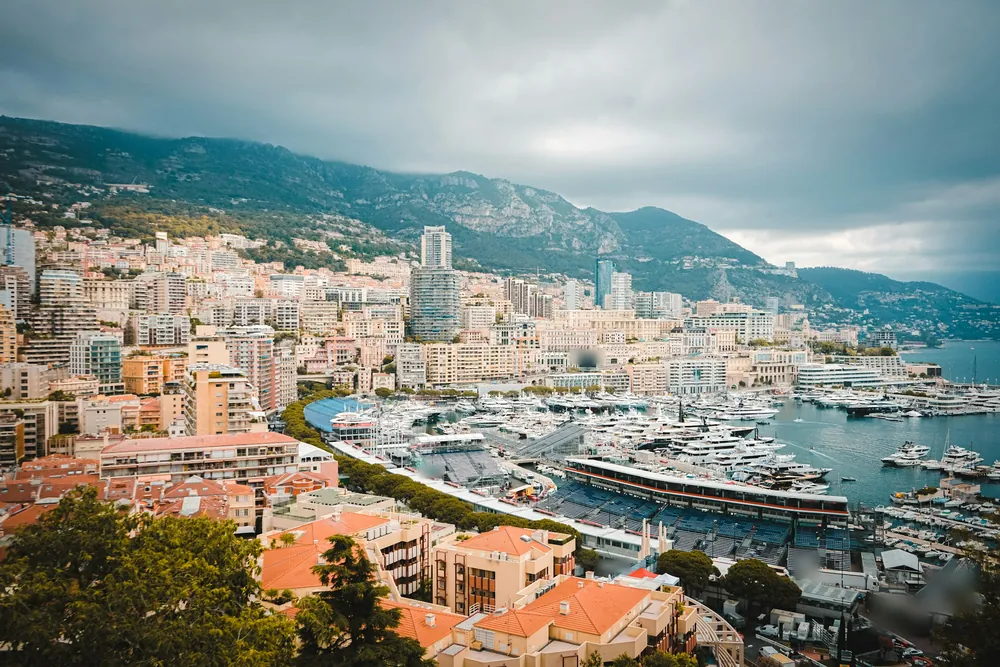 Monaco vue des hauteurs : le port Hercule rempli de yachts, les tribunes du Grand Prix et les immeubles de Monte-Carlo au pied de la montagne.