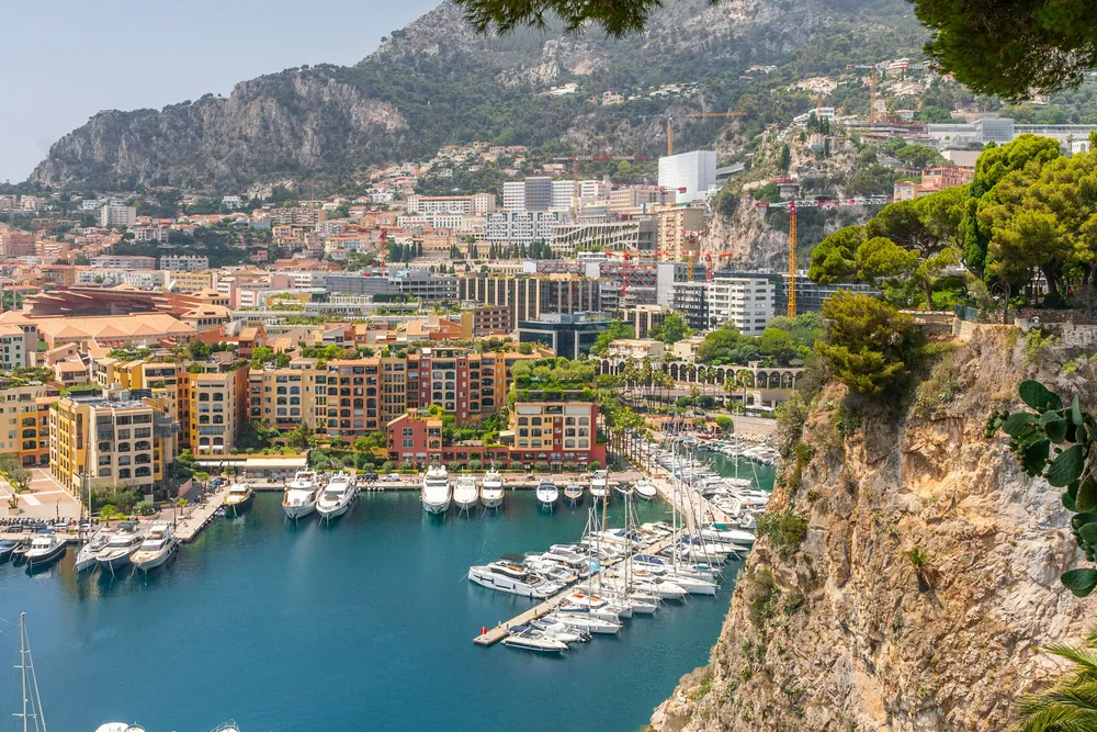 Le port de Fontvieille à Monaco, ses yachts et ses immeubles ocre au pied de la montagne, vus du Rocher sous les pins.