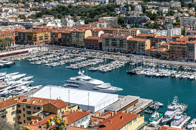 Un grand yacht à quai dans le port Lympia de Nice, devant les bateaux de la marina et les façades ocre du quai, vus de la colline du Château.